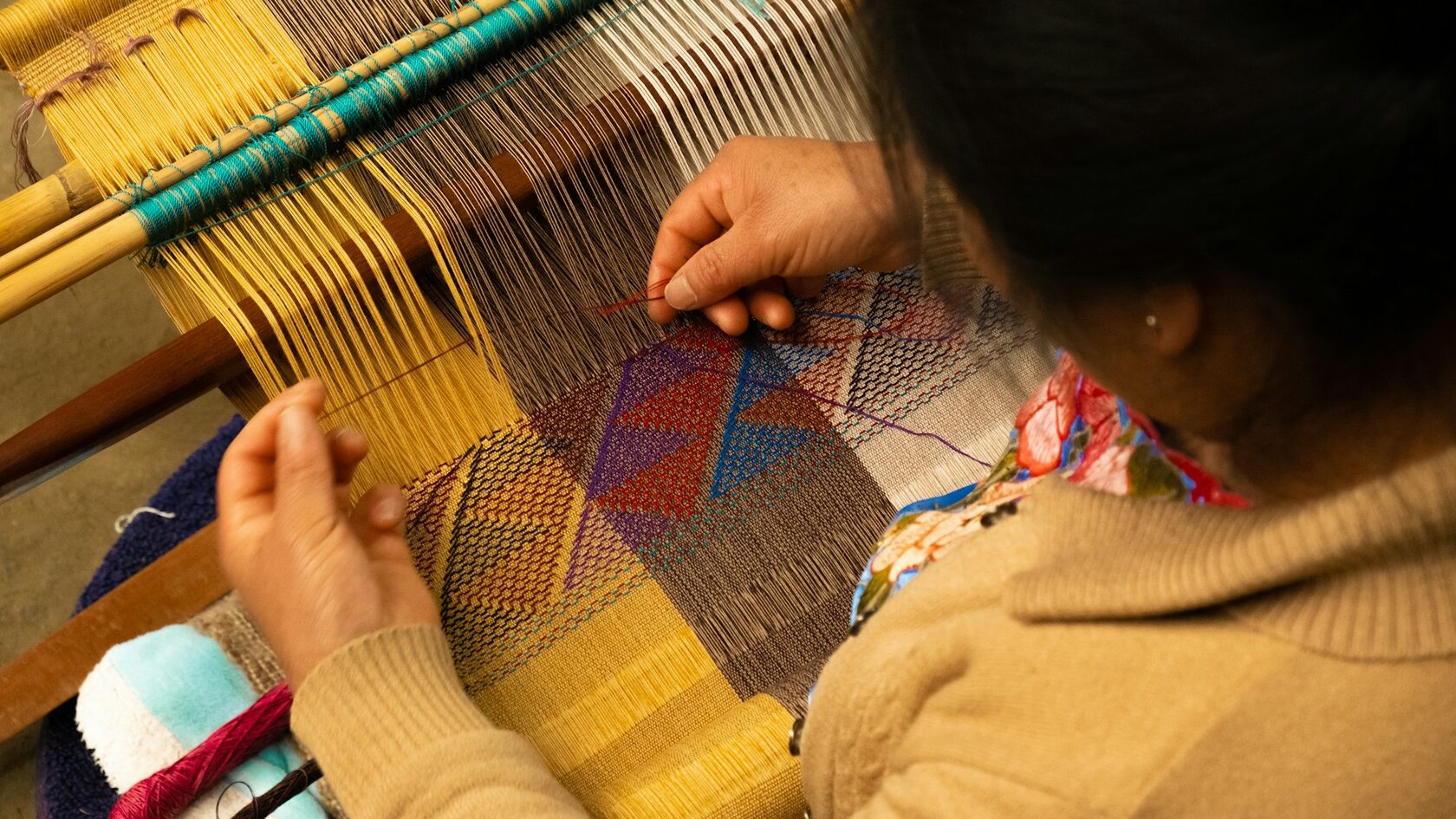 Hands weaving a colourful textile