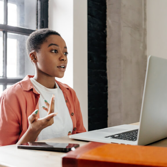 young black woman talking in front of her laptop, on an online meeting, with movement in her hands expressing her point