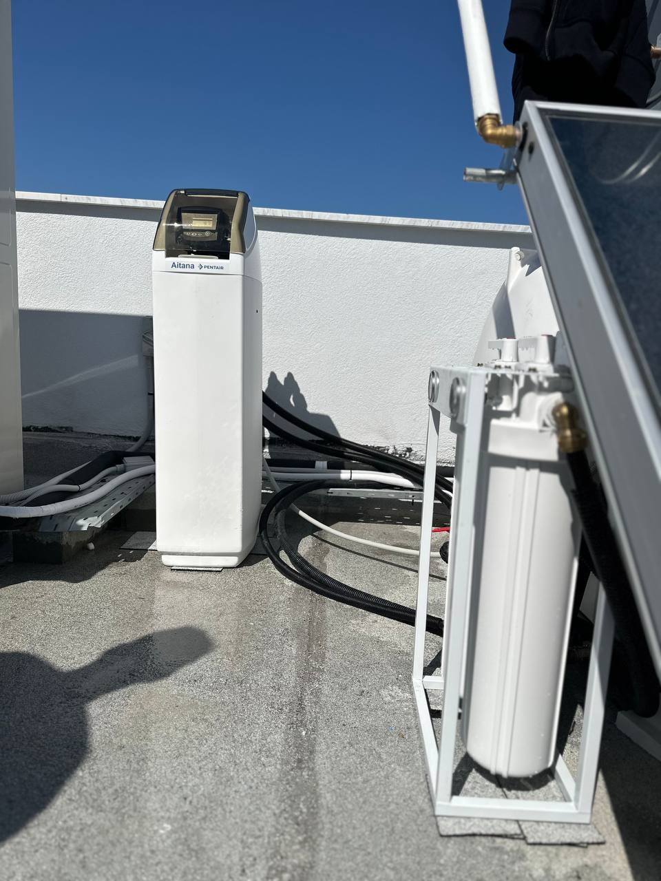 Water softening cylinder connected to the cold water inlet of a solar water heater panel on a roof.