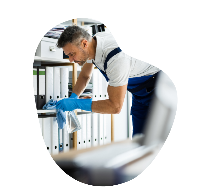 A male cleaner wearing blue gloves cleaning shelves in an office environment.