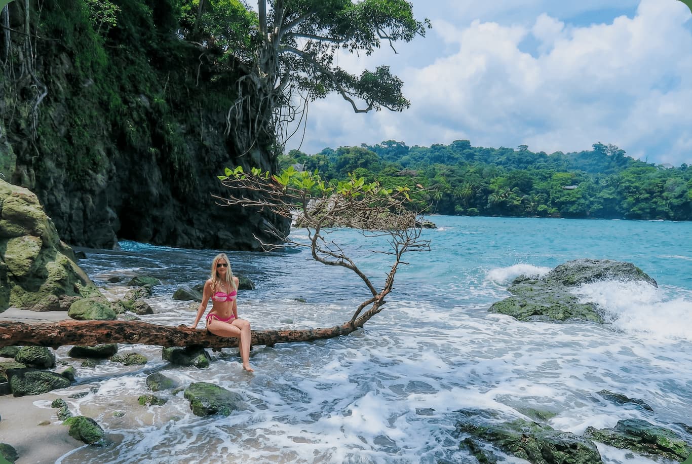 Guest sitting on a driftwood tree over the surf at Wild Makanda Beach