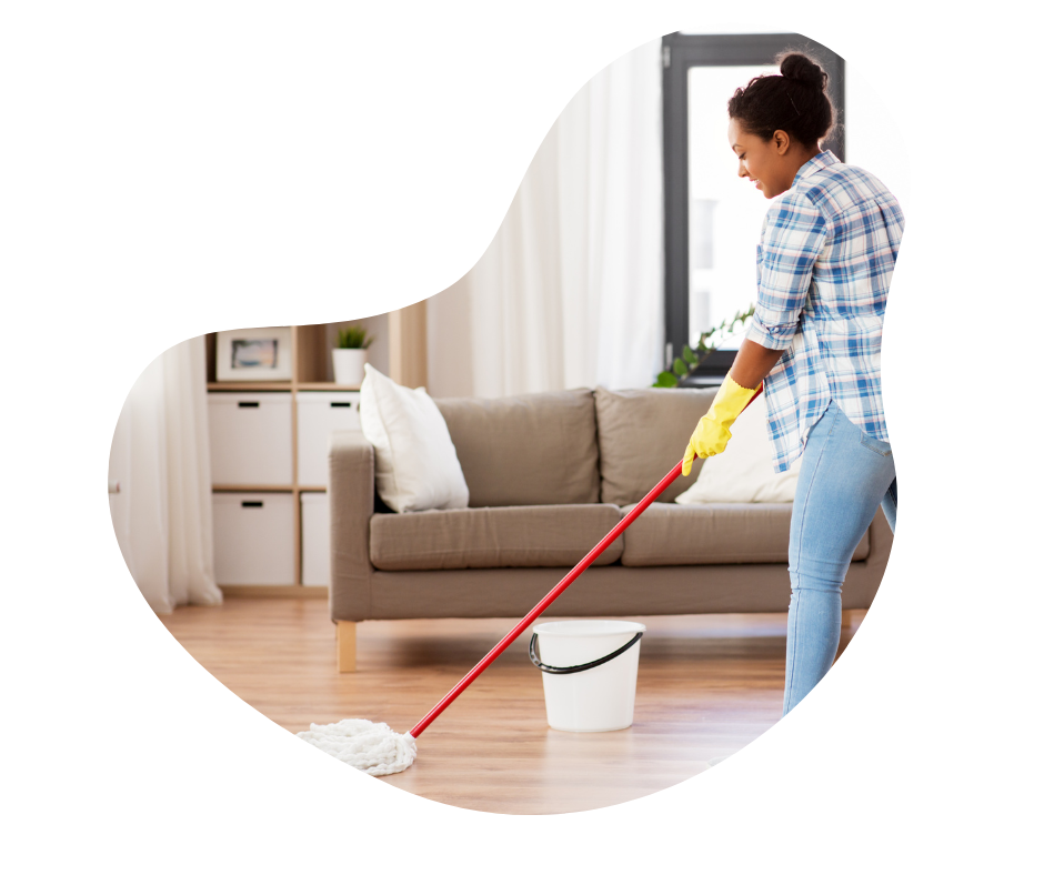 Female cleaner mopping a wooden floor in a lounge setting, with a sofa and book shelf behind her..