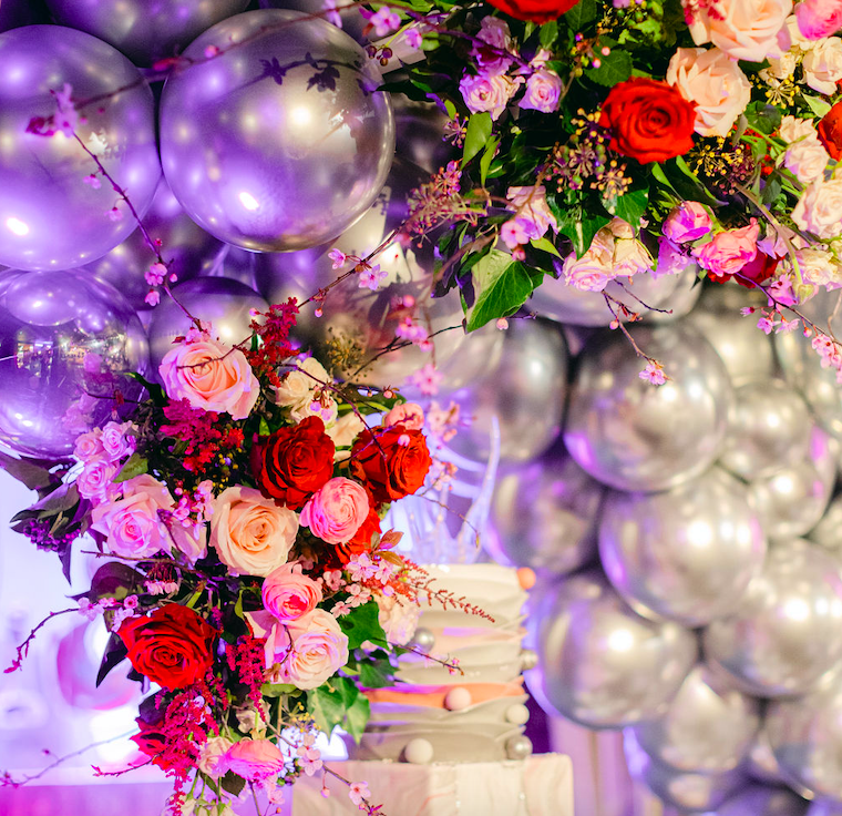 Mother and two daughters in pink dresses pose in front of a flower wall at family photo session