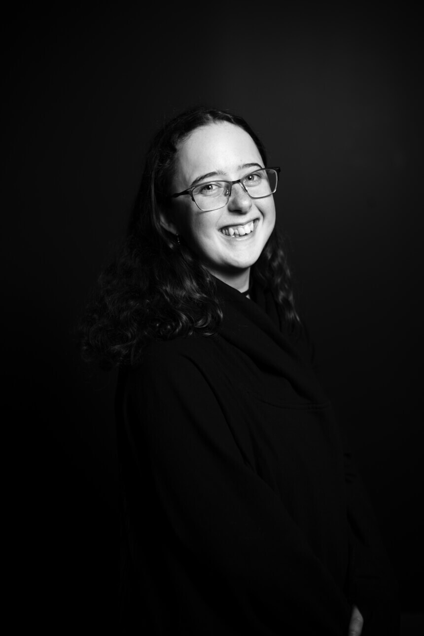 Black and white portrait of a young woman wearing glasses and smiling at the camera