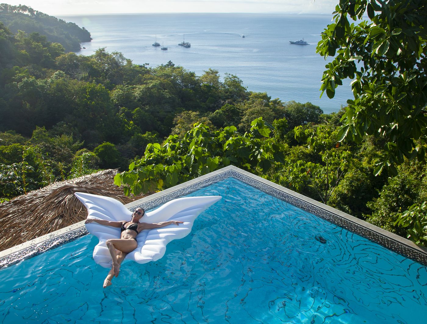 Guest floating on a butterfly lilo in the infinity pool, the Pacific beyond — Makanda