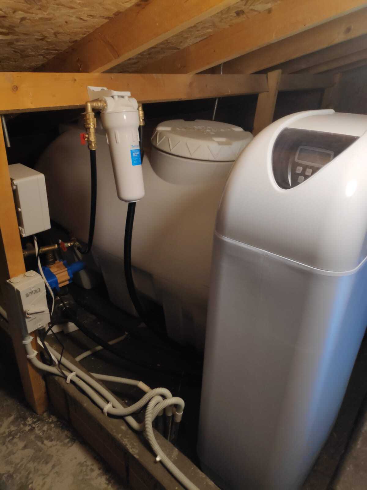 На картинке изображено реализованный проект установки системы умягчения воды в техническом помещении дома: умягчитель подключен после накопительного бака и насоса, выполнена профессиональная разводка труб и сервисных клапанов.