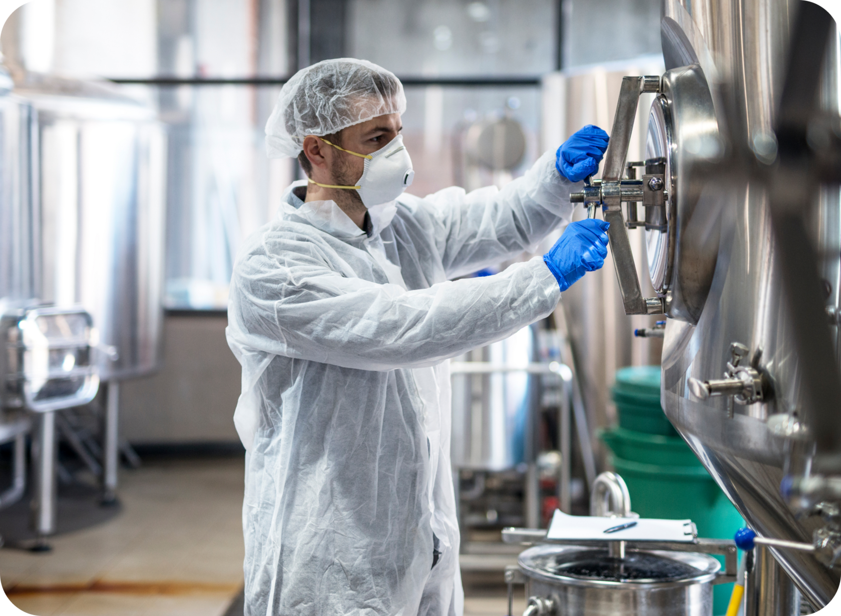 Technician in protective gear working with stainless steel equipment at The Base Beverage production facility, ensuring certified food safety standards