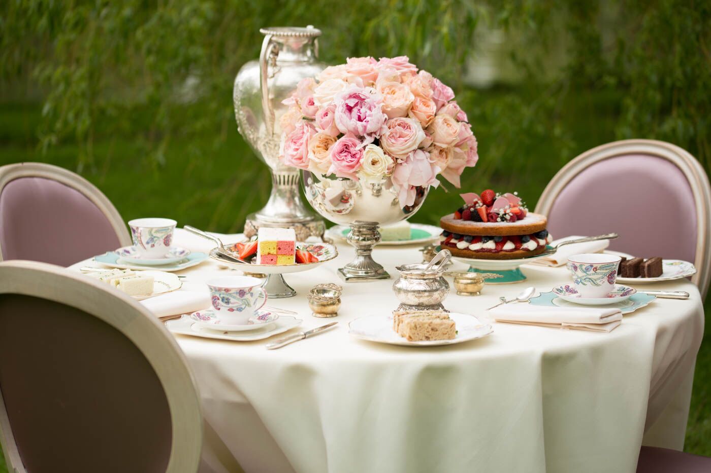 Table setting for a traditional British afternoon tea with blush pink flower arrangements, Victoria sponge cake and other desserts