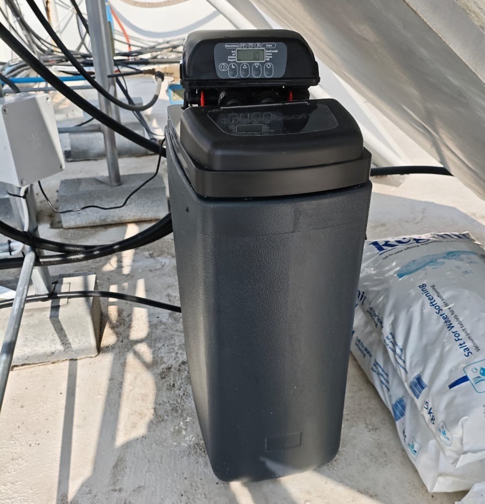 Compact cabinet-style water softener system secured on a flat roof in Limassol against a white wall.