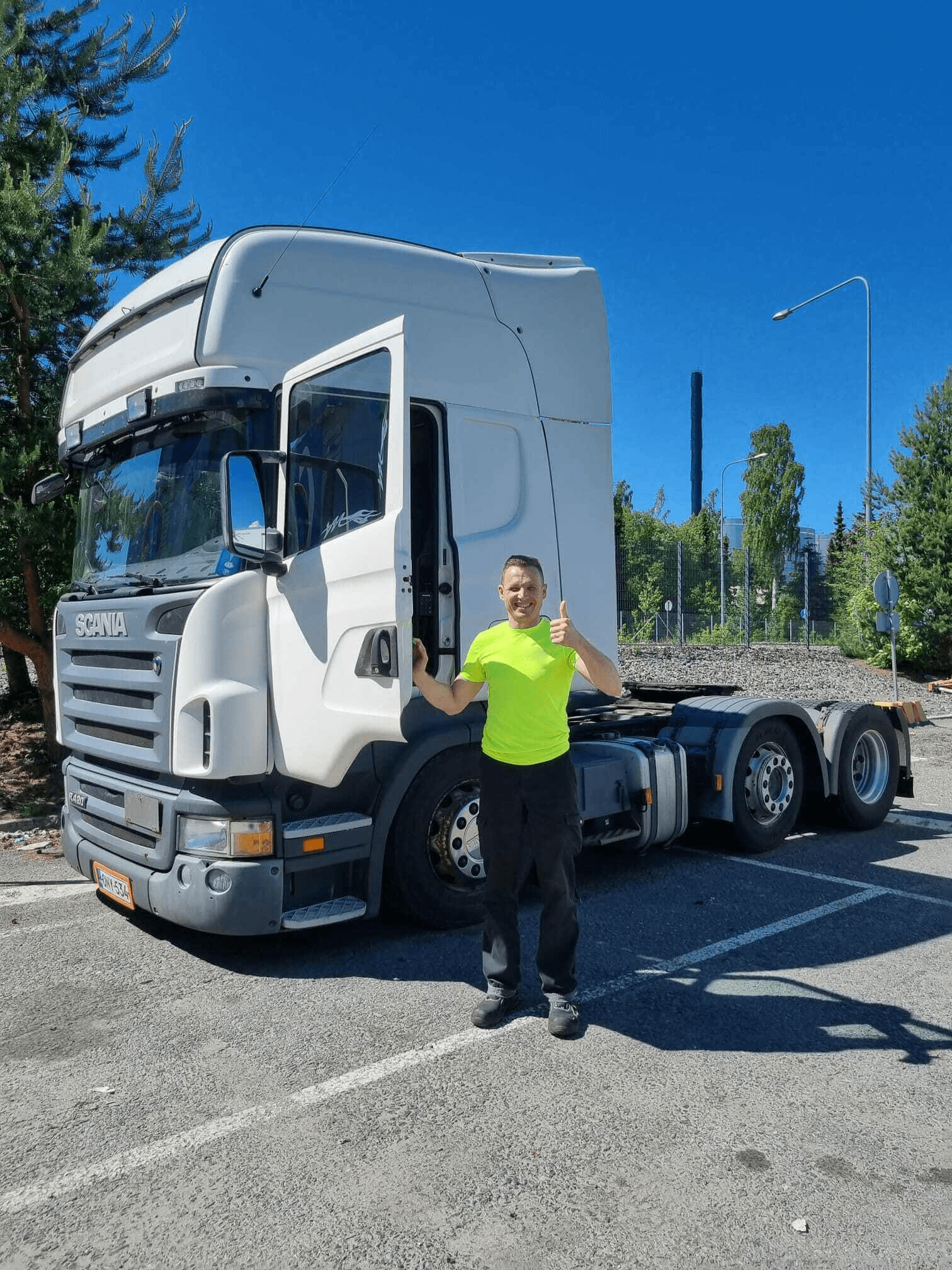 Mies keltaisessa paidassa seisoo parkkipaikalla kuorma-auton ohjaamon lähellä