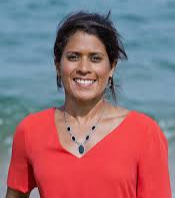  Portrait of Dr. Asha de Vos, Sri Lankan marine biologist, standing in front of the ocean wearing a red top and a black stone necklace, smiling confidently