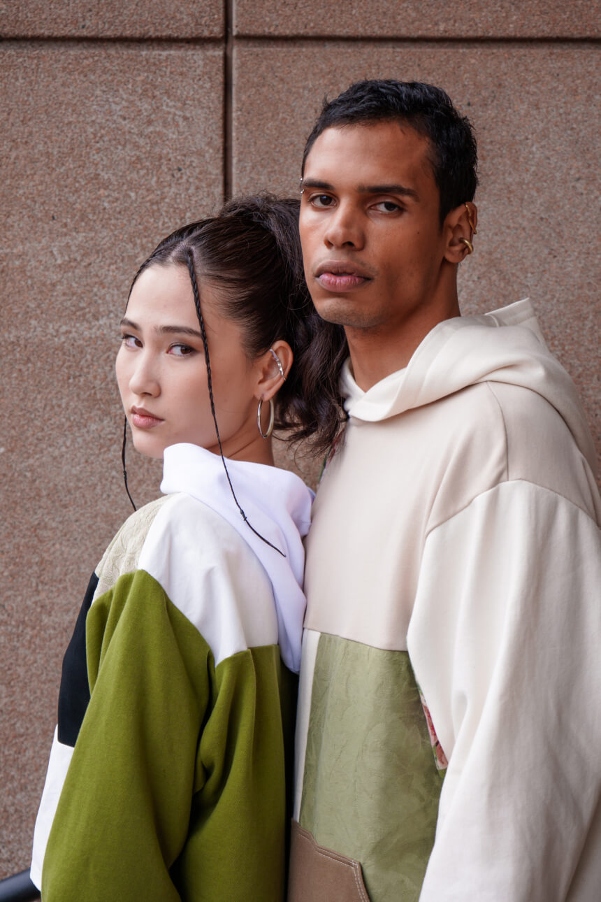 Two models posing in green and beige patchwork hoodies