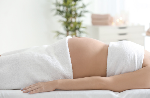 Беременная женщина лежит на массажном столе.