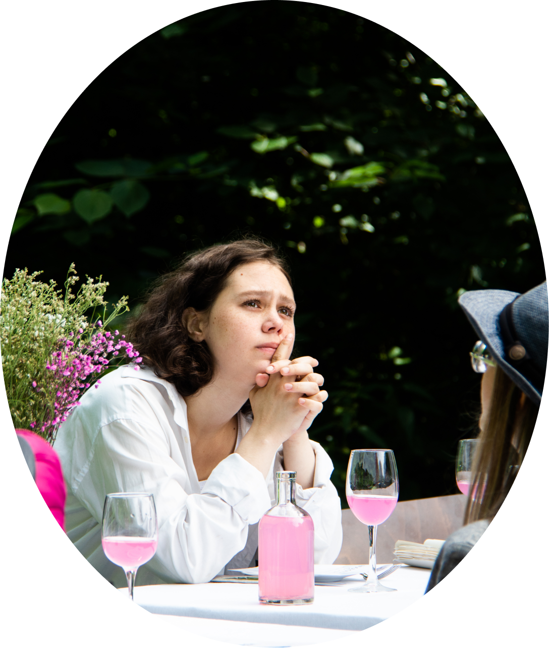 Actress thinks at the table in the park. There is a glass of rose water on the table