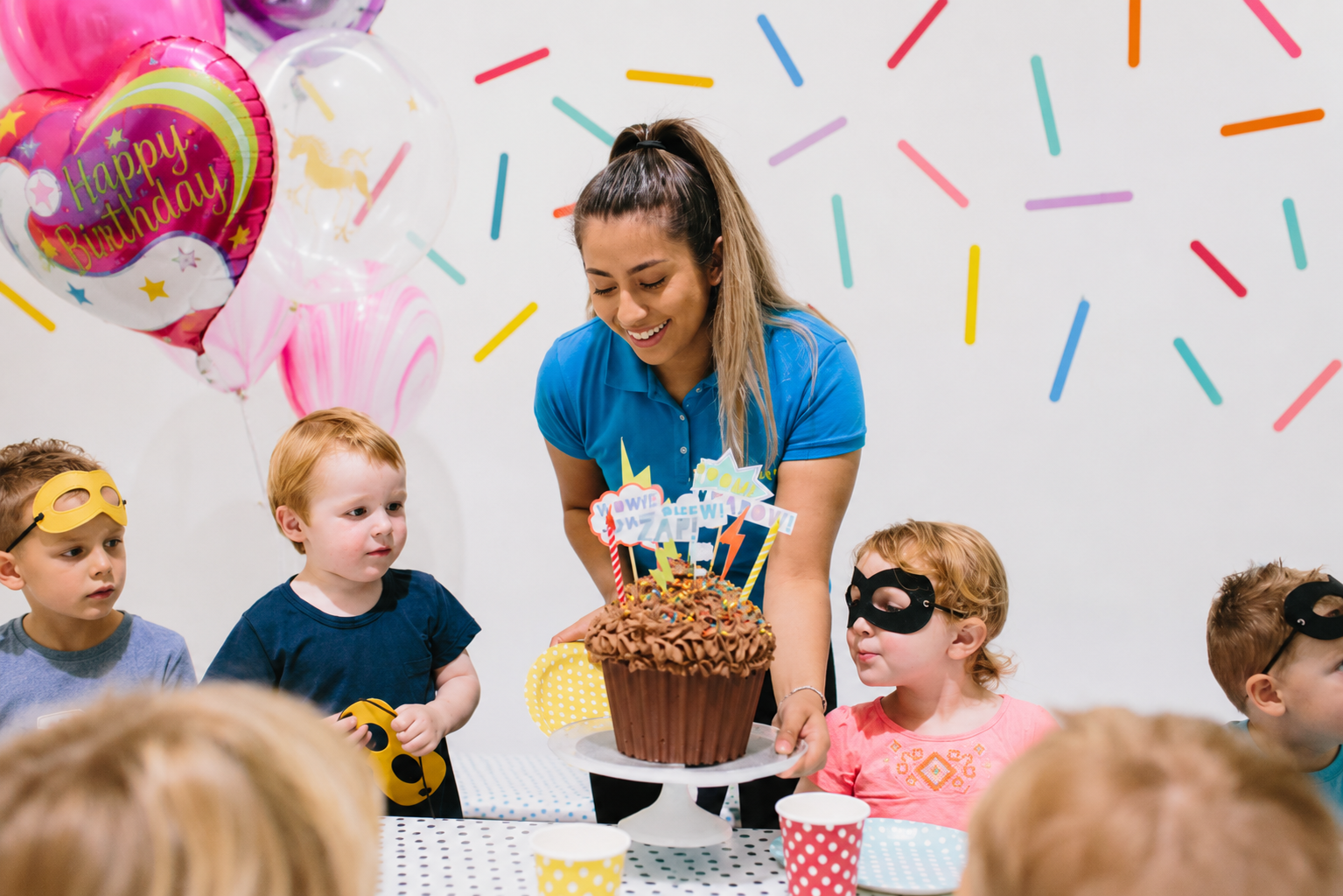 Tumbles themed birthday party with unicorn balloons, a giant purple cupcake cake and children with party hats
