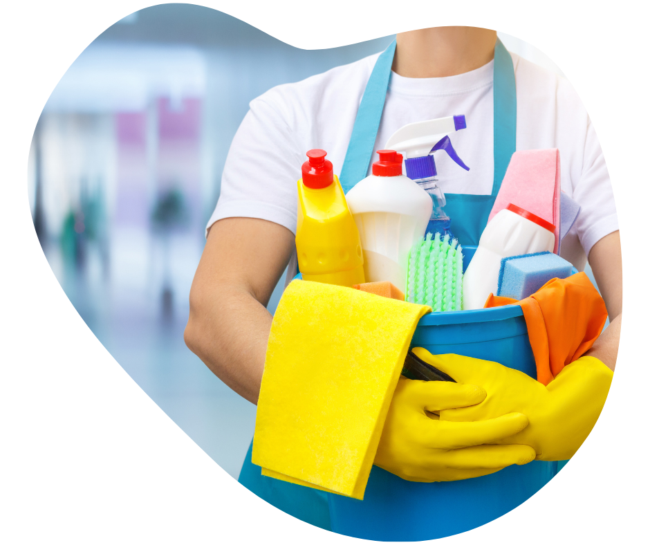 A male cleaner, wearing yellow cleaning gloves,holding a blue bucket with a variety of cleaning products (clothes, brushes, spray bottles, sponges etc...) in an office setting.