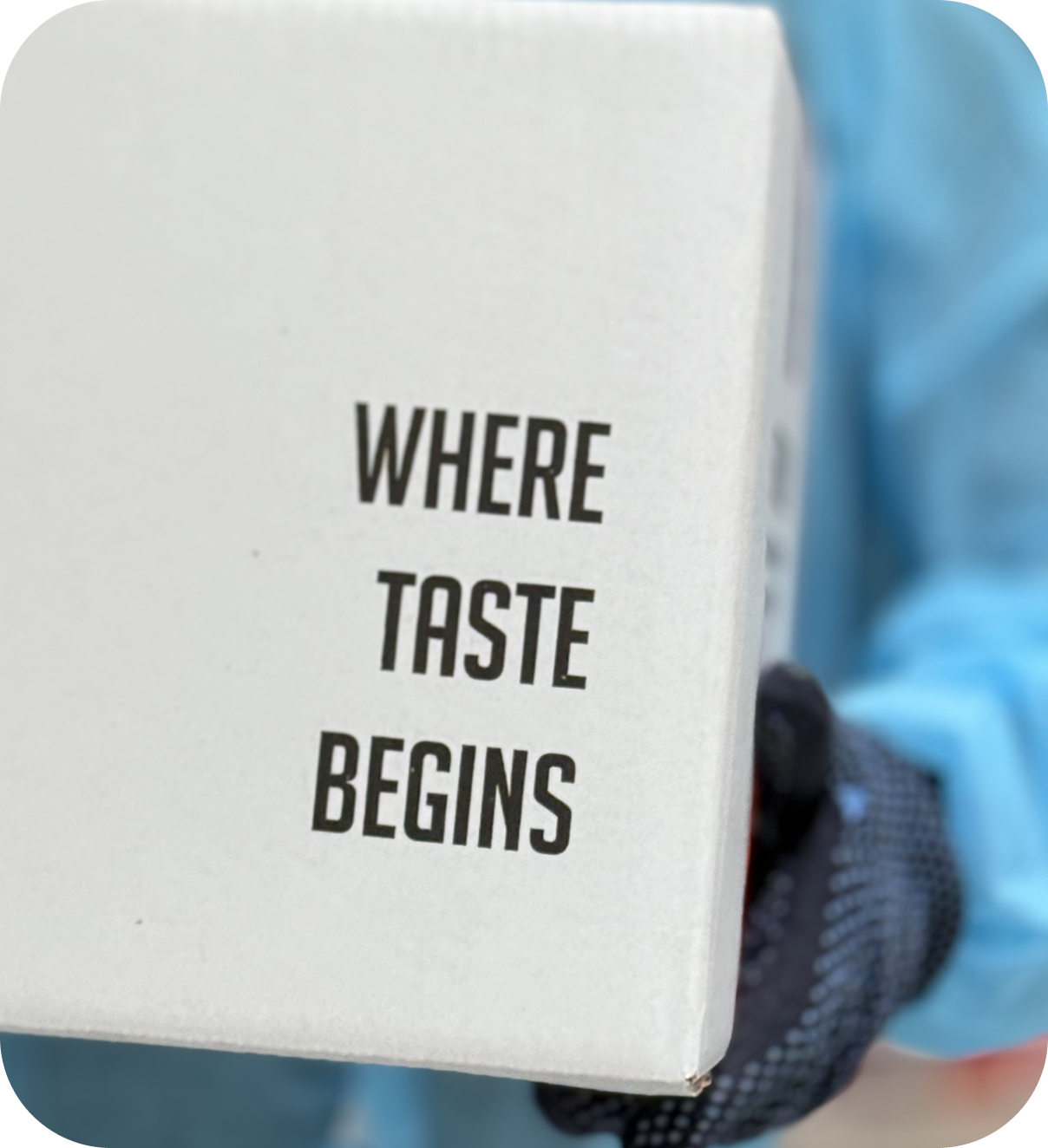 Close-up of branded shipping box from The Base Beverage with slogan "Where Taste Begins" held by staff in production gear