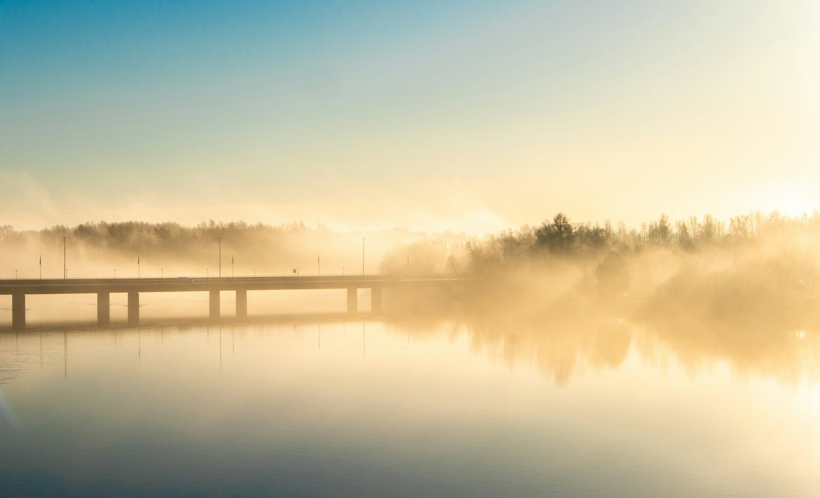 Puente de piedra sobre aguas tranquilas al amanecer, niebla baja